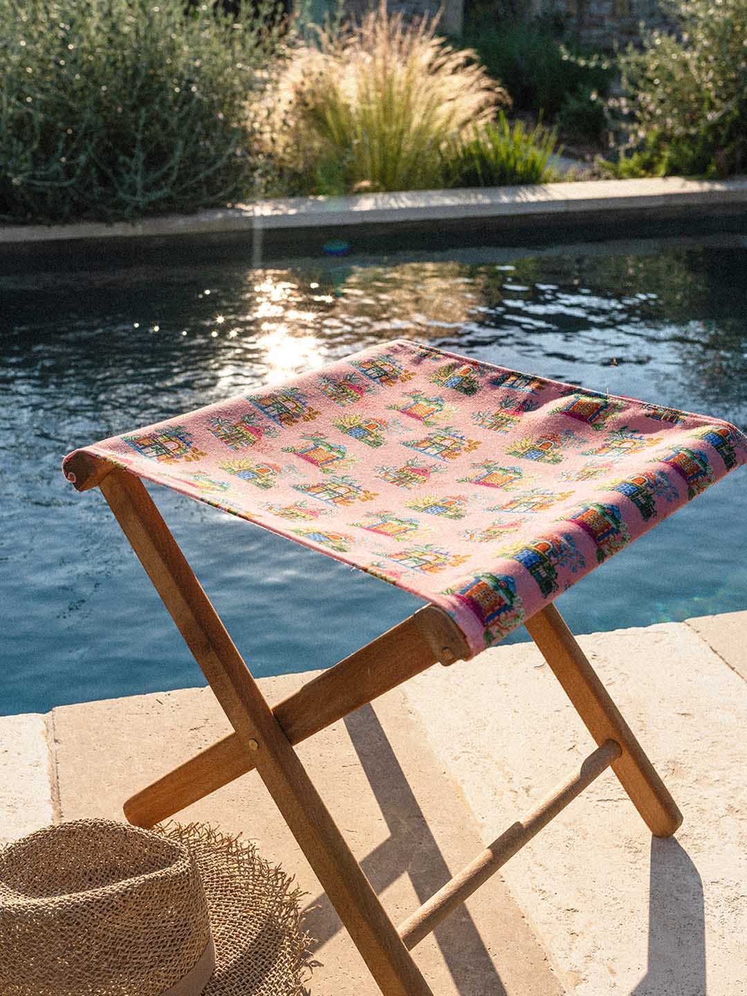 Tabouret pliant en bois à assise en toile fleurie au bord d'une piscine